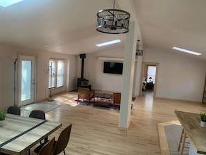 Amplia sala de estar con techo alto, una lámpara de metal negro, una chimenea, un televisor montado en la pared y un comedor con mesa y sillas.