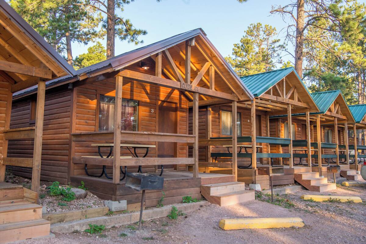 A row of log cabins with wooden benches and picnic tables outside.