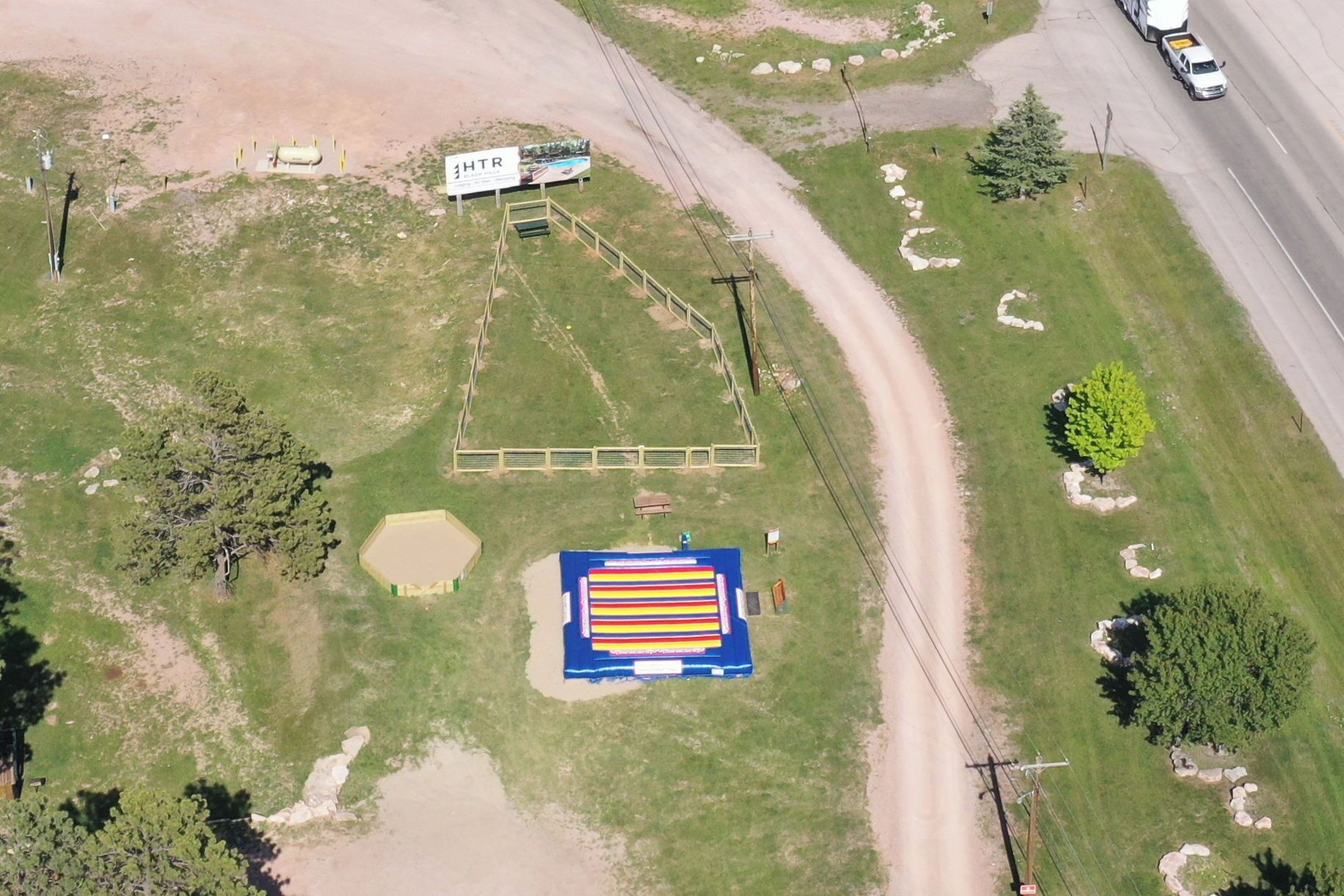 An aerial view of a property with a fenced area, a large rectangular building, and a road with vehicles.