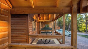 Eine Holzhütte mit überdachter Veranda, einem Picknicktisch und einem geparkten Auto.