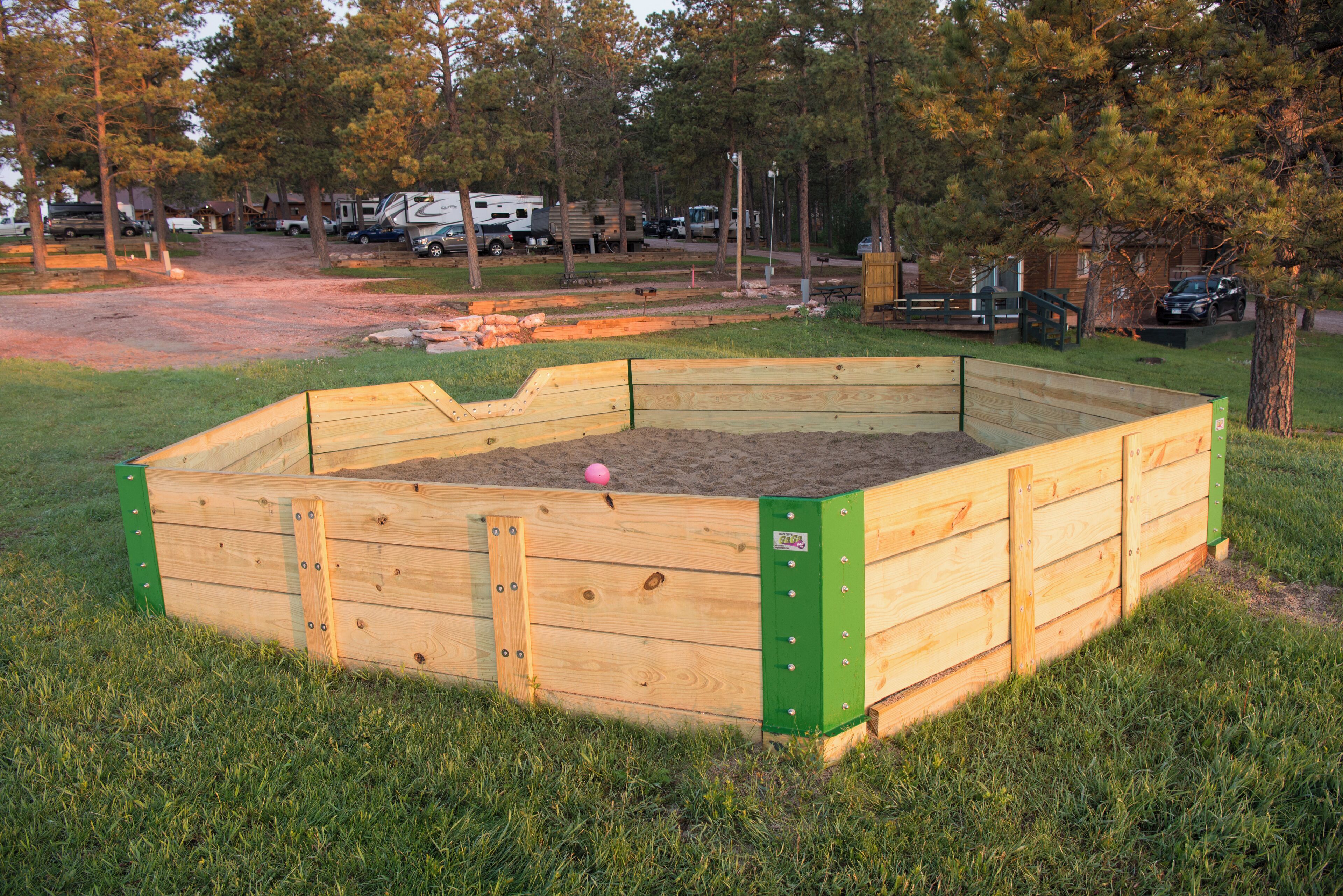 A wooden raised garden bed with a green metal frame, surrounded by grass.
