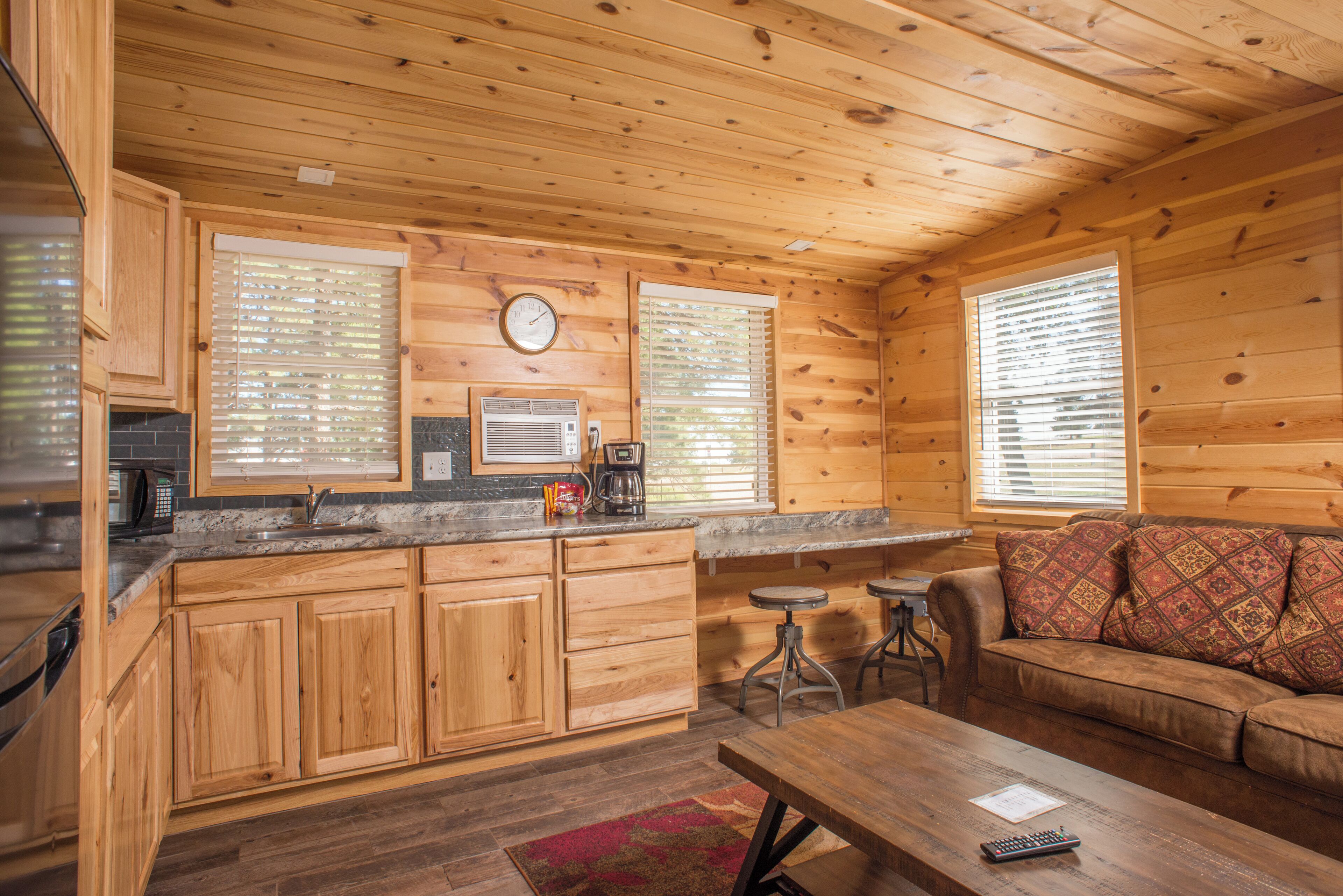 A wooden cabin interior with a kitchen, dining area, and a sofa.