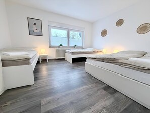 Un dormitorio con dos camas, un radiador, una ventana con persianas y detalles decorativos en la pared.