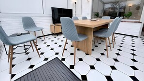Ein Essbereich mit einem Holztisch, vier Stühlen, einem Fernseher und einem gemusterten Boden.