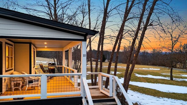 A house with a porch, outdoor seating, and a view of trees and a sunset. - Serene Fairview Escape (Fairview)