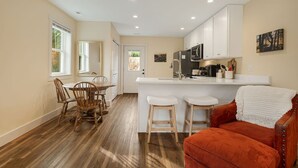 A modern kitchen with white cabinets, a central island with stools, and a dining area with wooden chairs. - Serene Fairview Escape (Fairview)