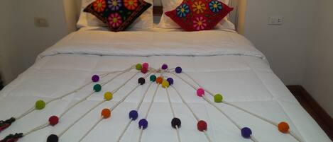 Una cama con edredón blanco y pompones de colores dispuestos en un diseño.
