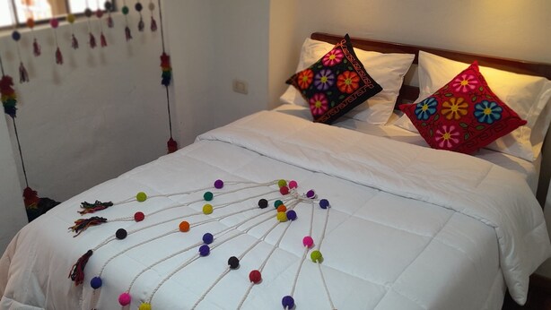 Un lit avec une literie blanche, des coussins colorés et une composition décorative de pompons sur la couvre-lit.