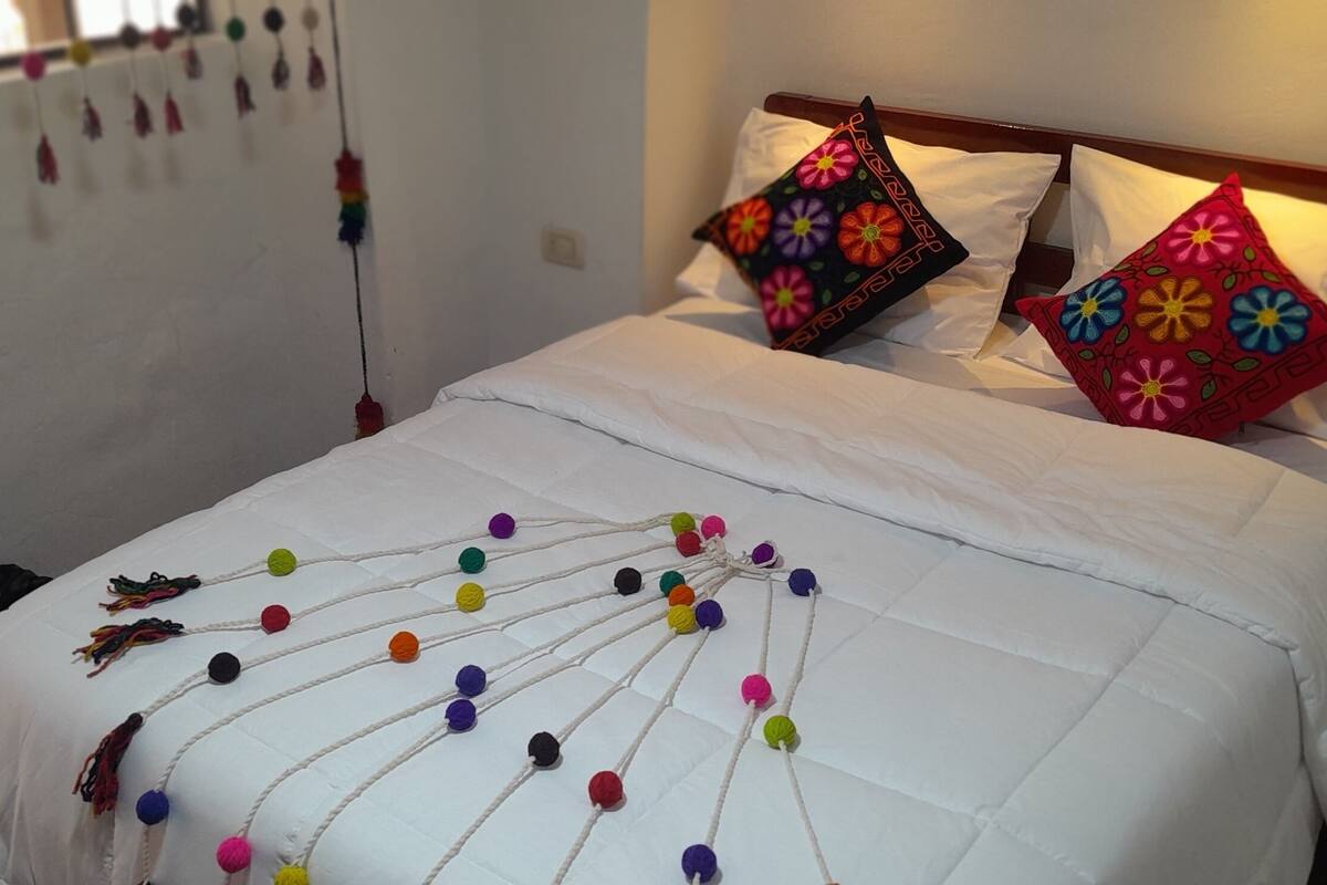 A bed with white bedding, colorful pillows, and a decorative pom-pom arrangement on the bedspread.