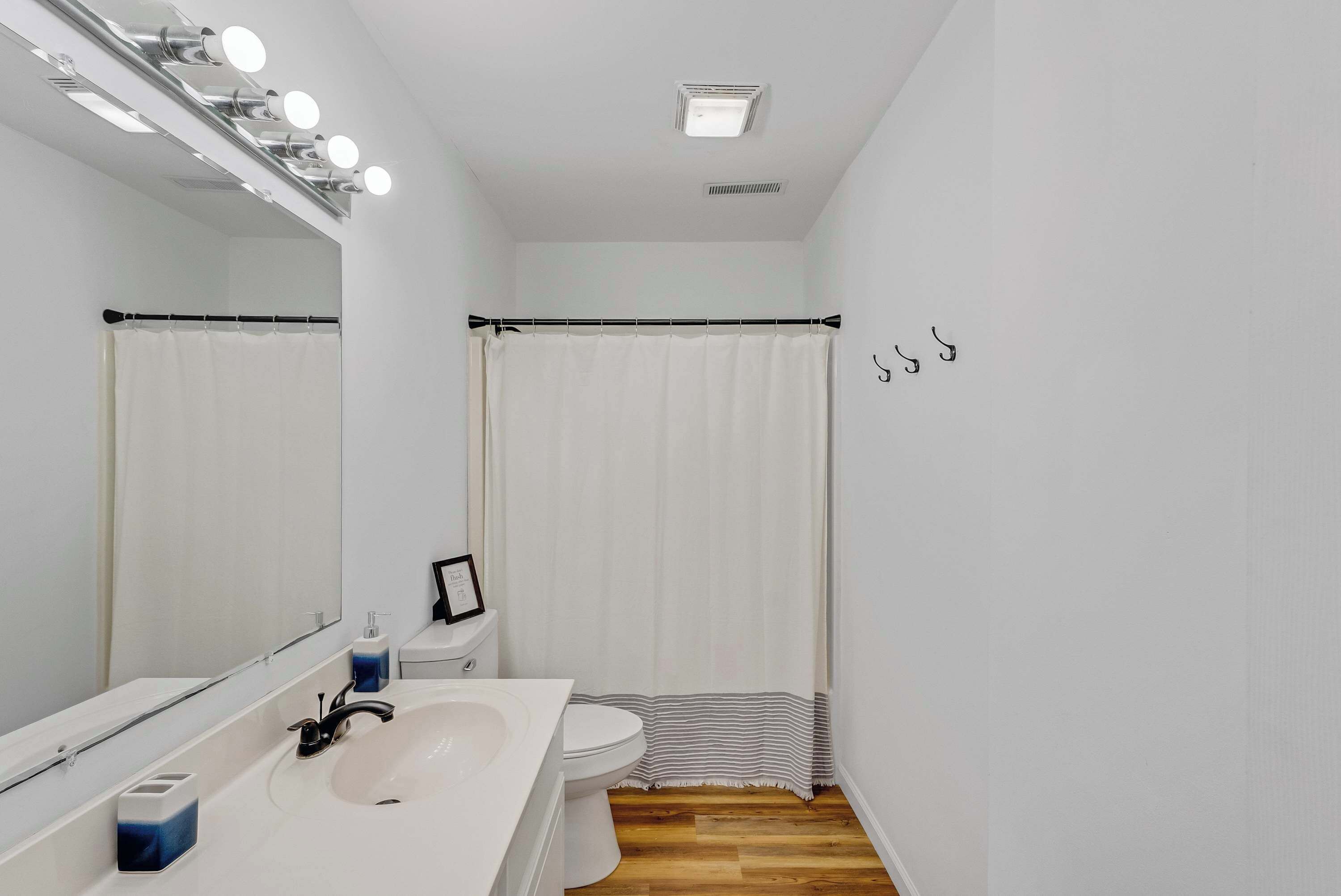 Une salle de bain avec un lavabo blanc, un miroir et des toilettes. On y trouve un rideau de douche et un tapis de bain à rayures.