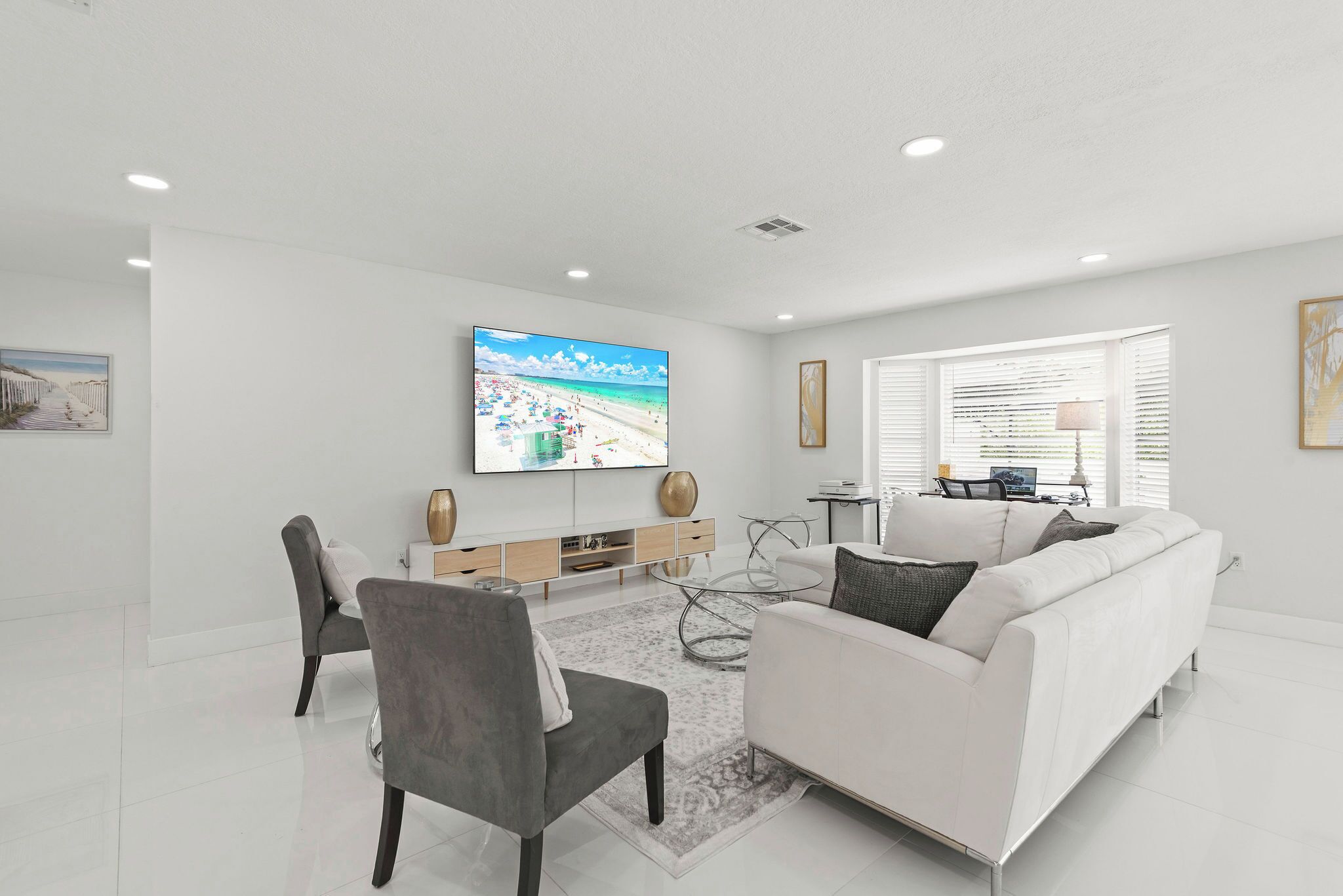 Uma sala de estar moderna com um sofá branco, uma mesa de centro de vidro e uma TV de tela plana fixada na parede.