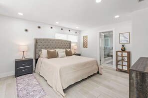 A bedroom with a large bed, bedside tables, a nightstand, a rug, a wooden cabinet, and a glass shower enclosure. - Charming 3BR/2BA Pool Home in Sarasota, Total Comfort, Minutes to Siesta Key! (Sarasota)