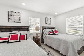 Quarto com duas camas, roupa de cama branca, almofadas vermelhas e pretas, e arte abstrata nas paredes.