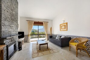 A living room with a fireplace, sofa, and wicker chair. - Villa 'Casa 54' with Private Terrace and Wi-Fi (Luz)
