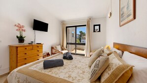 A bedroom with a bed, a dresser, a TV, a window with curtains, and a painting on the wall.
