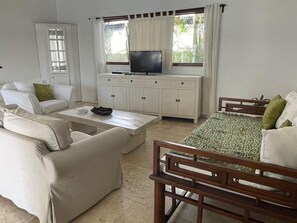 A room with a sofa, a wooden bed, a TV on a cabinet, and a window with curtains. - VILLA BALI 10 MINUTES FROM JUAN DOLIO BEACH (Playa Juan Dolio)