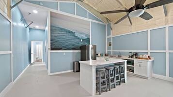 A modern kitchen with a central island, bar stools, and a ceiling fan.