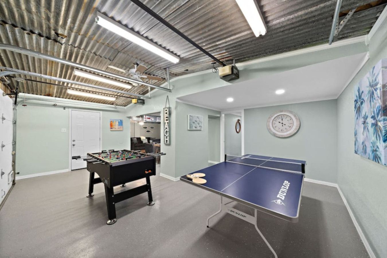 Una habitación con mesa de futbolín, mesa de ping pong, vigas a la vista y luminarias.