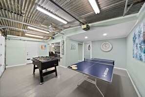 Una habitación con mesa de futbolín, mesa de ping pong, vigas a la vista y luminarias.