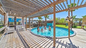 A covered swimming pool with a wooden deck and lounge chairs. - Family-Friendly Retreat with Pool & Outdoor Lounge (Kemah Area)