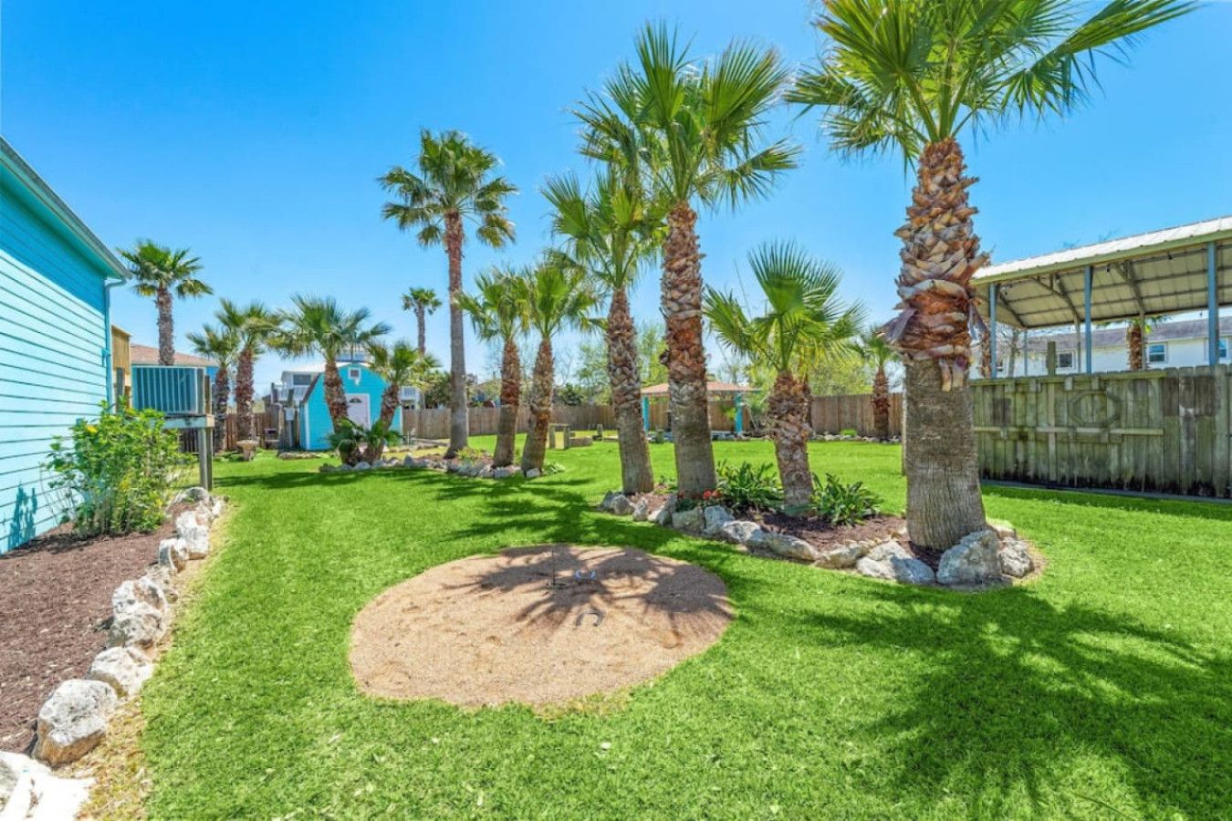 A backyard with a well-maintained lawn, palm trees, and a small circular garden area.