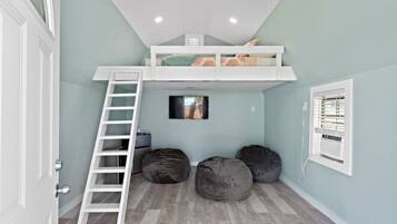 A room with a loft bed, a ladder, two bean bags, a small TV, and a window with blinds.