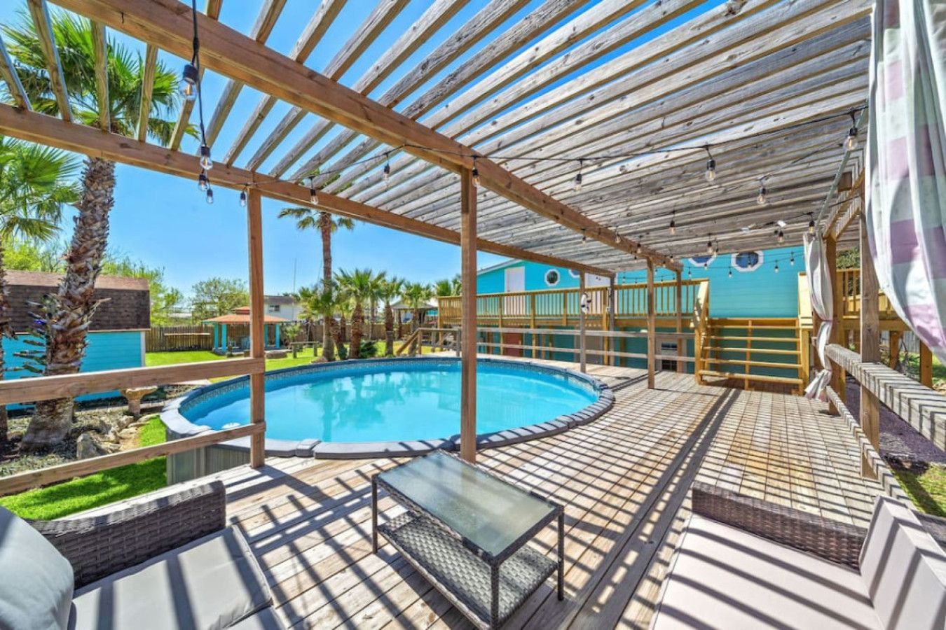 Una piscina exterior techada con un deck de madera, sillas de descanso y una mesa de vidrio.