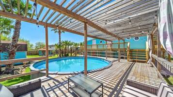 Una piscina exterior techada con un deck de madera, sillas de descanso y una mesa de vidrio.