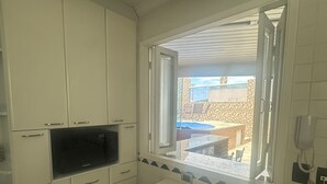 Et lille køkken med indbygget mikrobølgeovn, et spisebord med to stole og et vindue med udsigt til en patio.