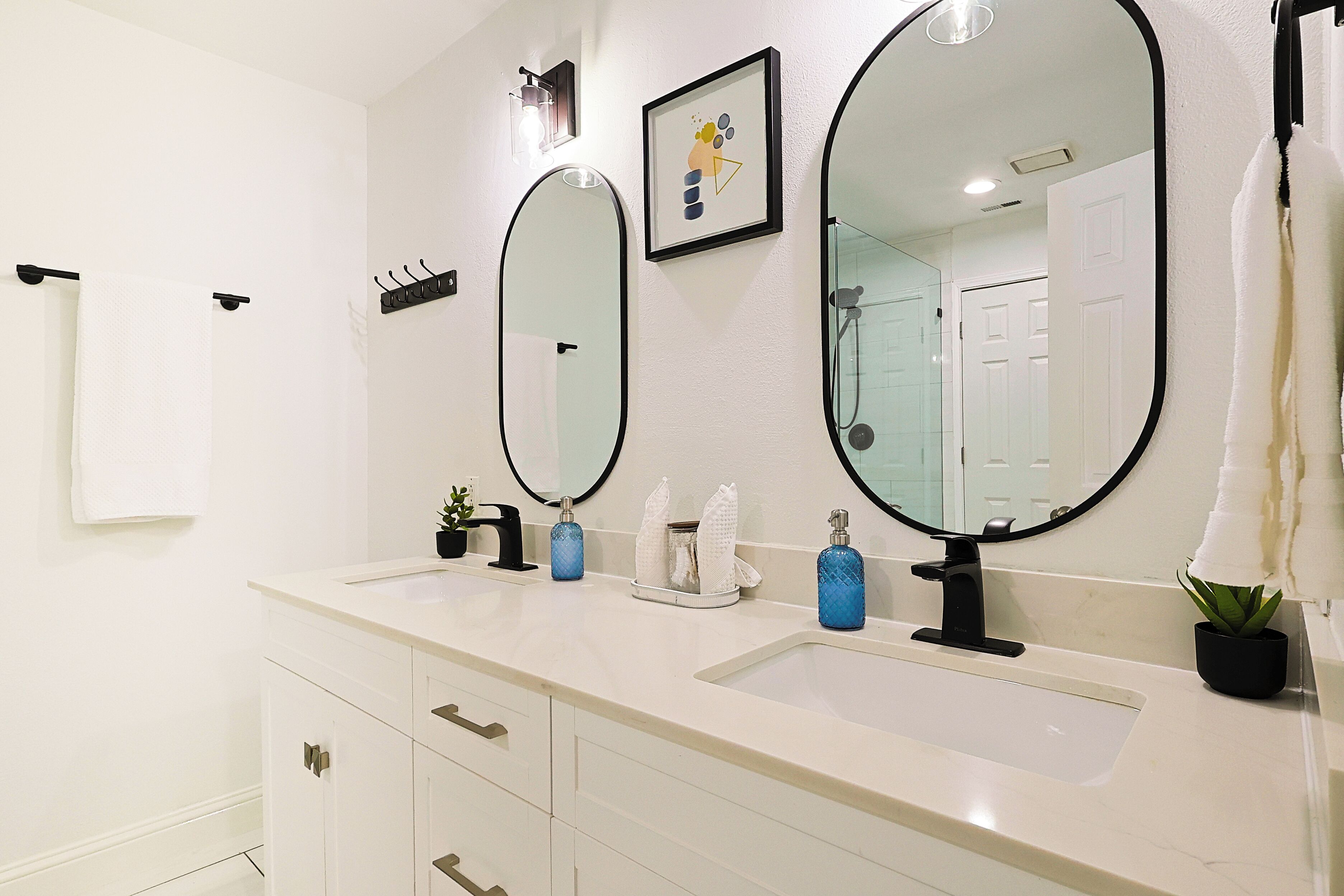 A modern bathroom with two sinks, large mirrors, a towel rack, and a small potted plant.