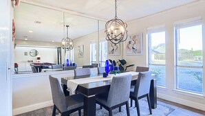 A dining area with a dark wooden table, grey upholstered chairs, and a chandelier. - Resort Style 4BR Plano Retreat - Pool, Spa & Entertainment (Plano)