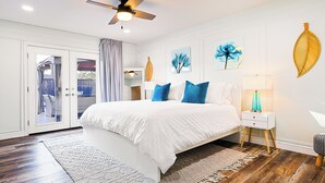 A bedroom with a large bed, a ceiling fan, a nightstand with a lamp, and artwork on the walls. - Resort Style 4BR Plano Retreat - Pool, Spa & Entertainment (Plano)