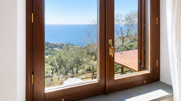 Ein Zimmer mit großem Fenster und Blick auf eine Küstenlandschaft, einer Holztür und einem eingebauten Lüftungsgitter.