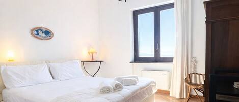 Un dormitorio con cama, lámparas de noche, una ventana con cortinas, un radiador y un armario de madera.