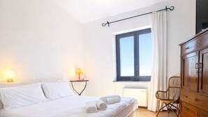 Ein Schlafzimmer mit Bett, Fenster, Stuhl, Kommode und Lampe.