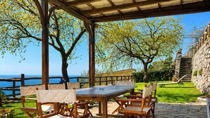 Eine Terrasse im Freien mit Holztisch und -stühlen, Steinboden und Blick aufs Meer.