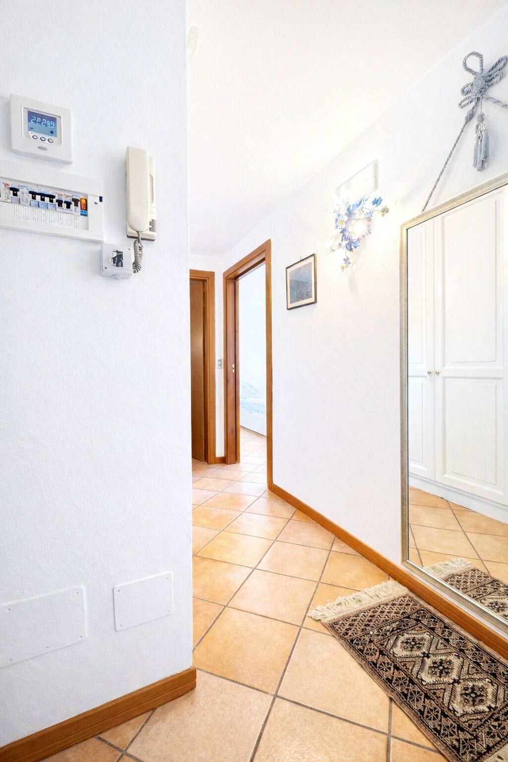 Un couloir avec un téléphone, un tableau électrique et une porte donnant sur une autre pièce.