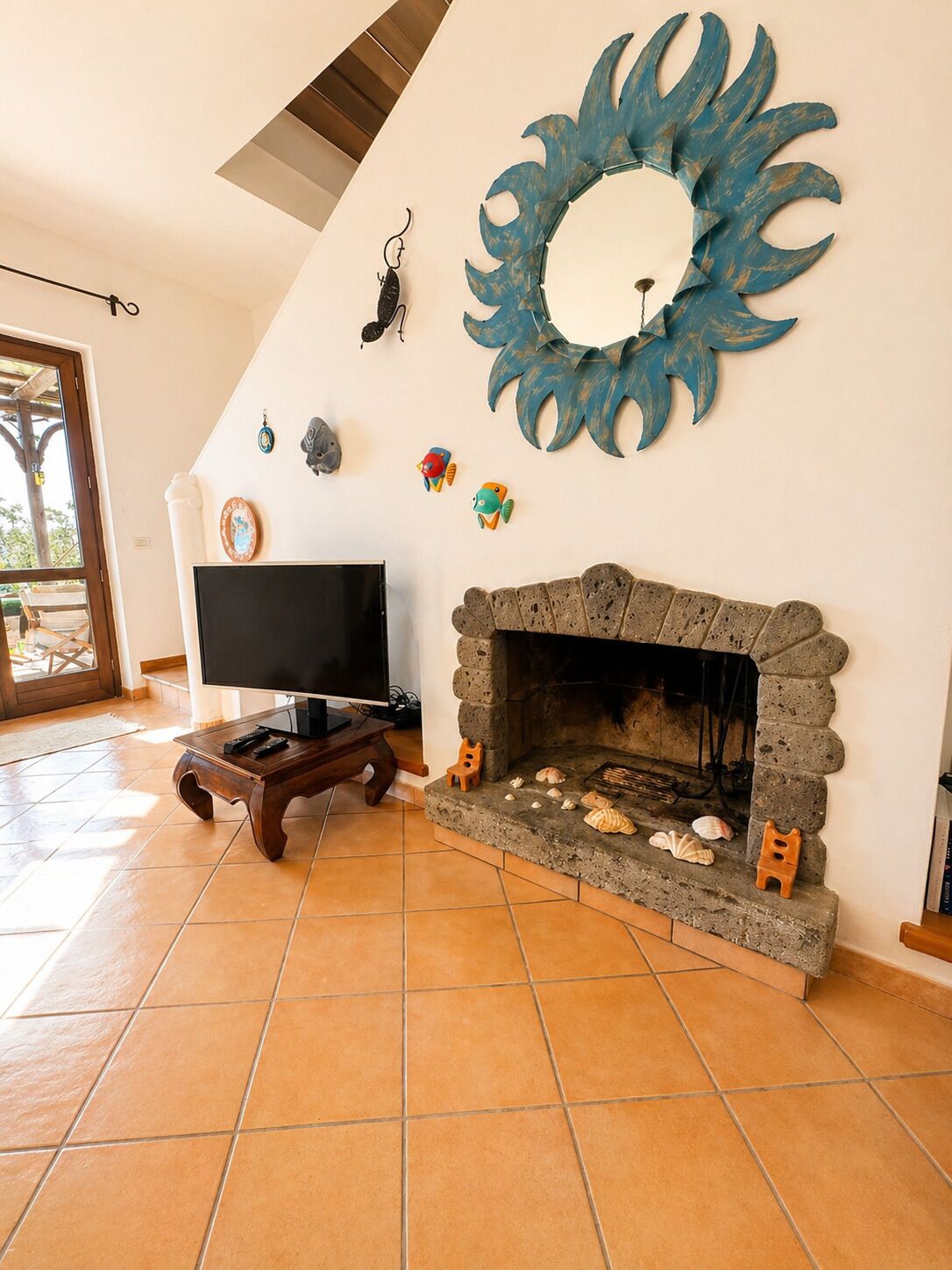 Un salón con chimenea de piedra, un televisor sobre un mueble bajo y un espejo decorativo grande.