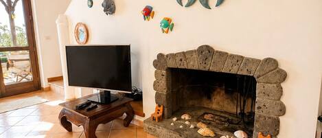 Un salón con chimenea de piedra, un televisor sobre un mueble bajo y un espejo decorativo grande.