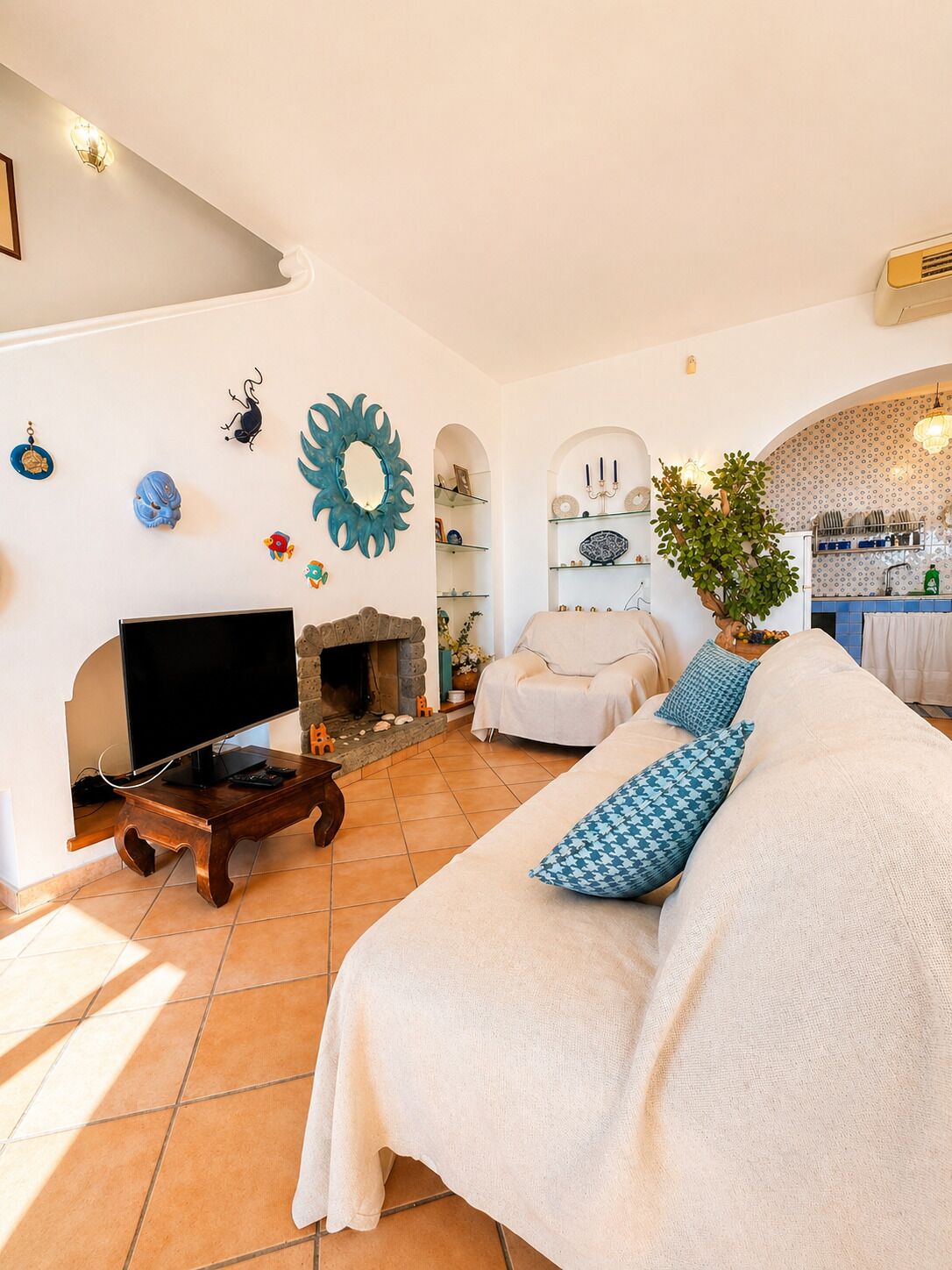 A living room with a TV, fireplace, sofa, and kitchen area.