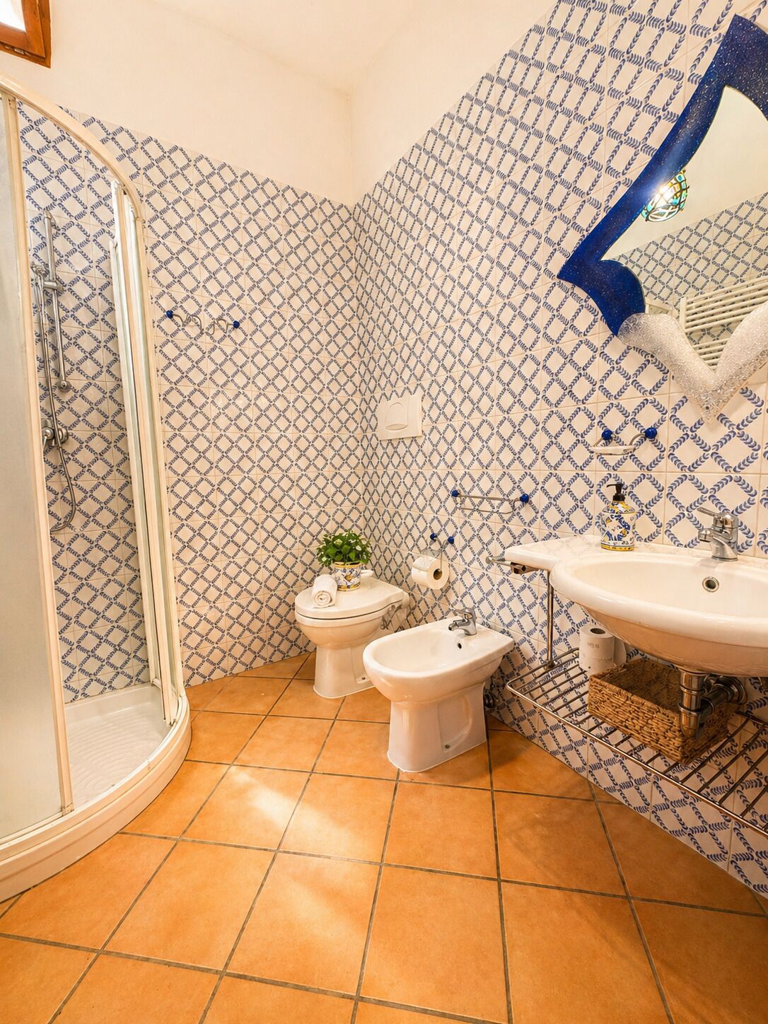 Ein Badezimmer mit Dusche, Toilette, Bidet und Waschbecken, alles mit gemusterten Fliesen.