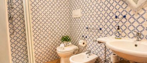 Ein Badezimmer mit Dusche, Toilette, Bidet und Waschbecken, alles mit gemusterten Fliesen.