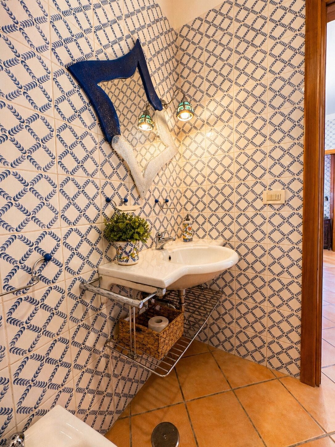 A bathroom with patterned tiles, a sink, a mirror, and a hanging towel rack.