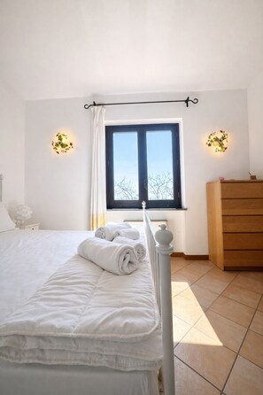 A bedroom with a bed, a dresser, a window with curtains, and wall-mounted lights. - Villa Laurì (Massa Lubrense)