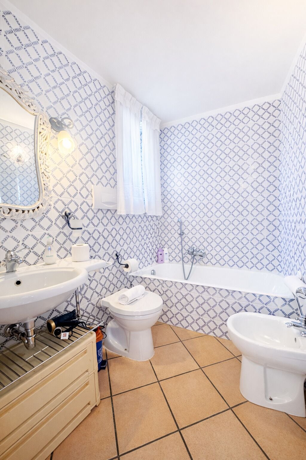 Une salle de bain avec un lavabo, des toilettes et une baignoire, un papier peint à motifs et un miroir.