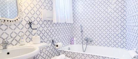 Une salle de bain avec un lavabo, des toilettes et une baignoire, un papier peint à motifs et un miroir.