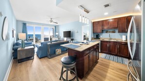 A modern kitchen with wooden cabinets, a central island, and a dining area with blue furniture. - Dolphin Views! Laketown Wharf - 7th Floor! (Panama City Beach)
