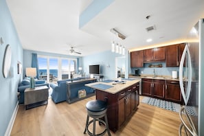 A modern kitchen with wooden cabinets, a central island, and a dining area with blue furniture. - Dolphin Views! Laketown Wharf - 7th Floor! (Panama City Beach)