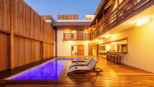 Un espace piscine extérieur moderne, doté d’une terrasse en bois, de deux chaises longues et d’un coin bar avec des sièges.