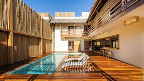 Un espace piscine doté d’un sol en bois, de chaises longues et d’un bar.